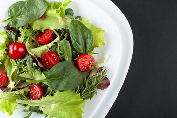Fresh mixed salad with cherry tomatoes on a black background. Top view.