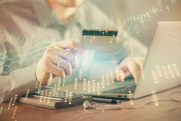 Double exposure of man hands holding a credit card and Forex graph drawing. Stock trading and digital fintech in Internet E-commerce concept.