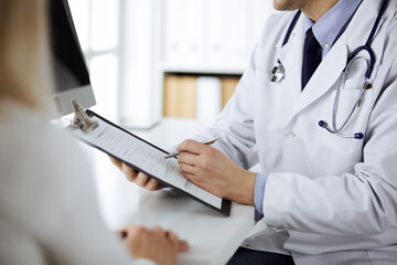 Unknown male doctor and patient woman discussing current health examination while sitting in clinic...
