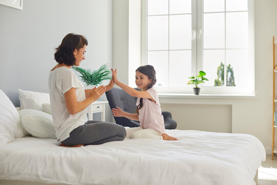 Happy mom and kid playing patty cake game sitting on comfortable bed in cozy light bedroom - Powered by Adobe