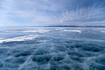 Beautiful blue ice surface with cracks net of frozen lake Hovsgol in Mongolia and snow covered mountain range and scenic sky on background. Winter landscape, copy space