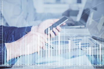 Double exposure of man's hands holding and using a digital device and forex graph drawing. Financial market concept.