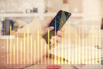 Double exposure of man's hands holding and using a digital device and forex graph drawing. Financial market concept.