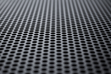 Perspective view on a the black metal surface with regular round holes. Industrial background...
