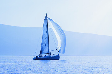 Fototapeta premium Sailing boat on water, blue tinting, silhouettes. Montenegro, Kotor Bay. Travel concept