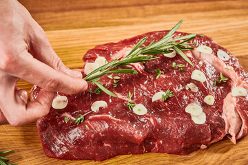 Raw beef steak seasoning with garlic slices and branch of fresh rosemary