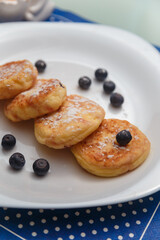 Traditional syrniki or cottage cheese pancakes with blueberries on white plate with blue napkin on kitchen table, close up.