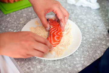 Woman rolling salmon fish in cornmeal before frying