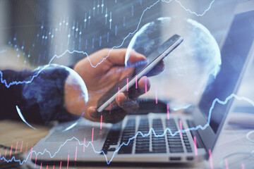 Double exposure of man's hands holding and using a phone and financial graph drawing. Analysis concept.