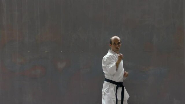 Young sportsman with blue belt doing formal exercises against street wall background