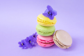 Colorful macaroons with little flowers one on top of each other on violet background.Small french cakes. Sweet and french macarons.