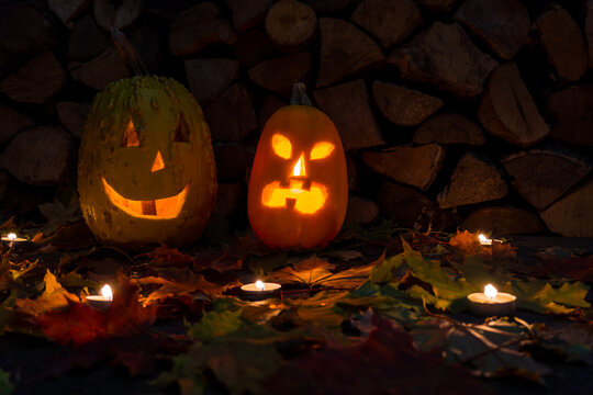 Two glowing pumpkins on halloween night with candles on a background of firewood and autumn foliage.