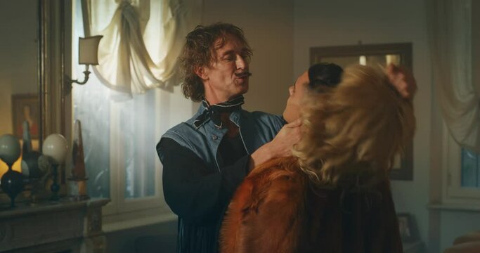 Cinematic shot of carefree happy smiling homosexual male gay dressed as cowboy is taking off a wig of his transgender woman partner and giving passionate kiss as sign of forever love at home.