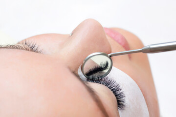 Fototapeta premium Eyelash extension procedure. Female eye with long eyelashes. Close up. mirror in the hands