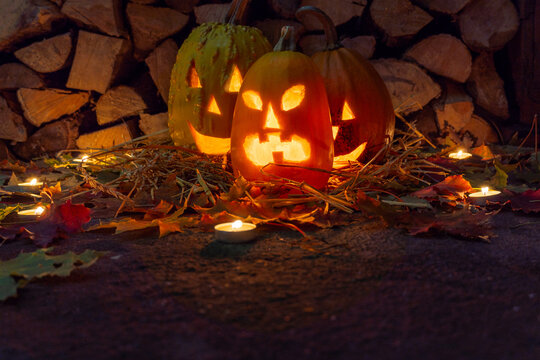 Three glowing pumpkins on halloween night with candles on a background of firewood and autumn foliage.