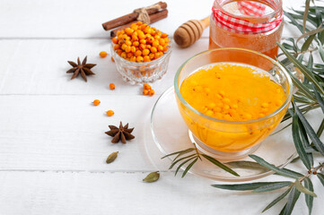 Colorful hot natural sea buckthorn tea in a glass cup, fresh raw berries and leaves, honey, anise and cinnamon sticks. Vitaminic healthy medicine drink. Concept of warm seasonal beverages.