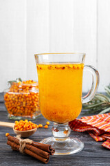 Colorful hot natural sea buckthorn tea in a glass cup, fresh raw berries  and cinnamon sticks. Vitaminic healthy medicine drink. Concept of warm seasonal beverages. Vertical view