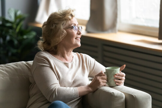 Peaceful Older Senior Granny In Eyeglasses Relaxing On Coffee With Cup Of Tea Coffee In Hands, Dreaming Of Future Or Recollecting Memories Alone At Home, Happy Retired Woman Enjoying Morning Ritual.