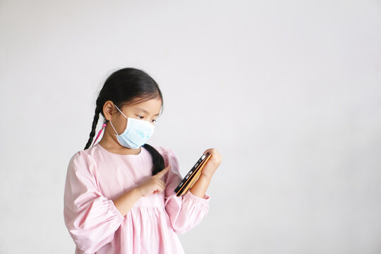 Asian Child Or Kid Girl Wearing Face Mask Protect Coronavirus To Learn From Home Or Study Online On Computer Tablet And Communication Touch Screen Or People Play Smartphone On White Space Background