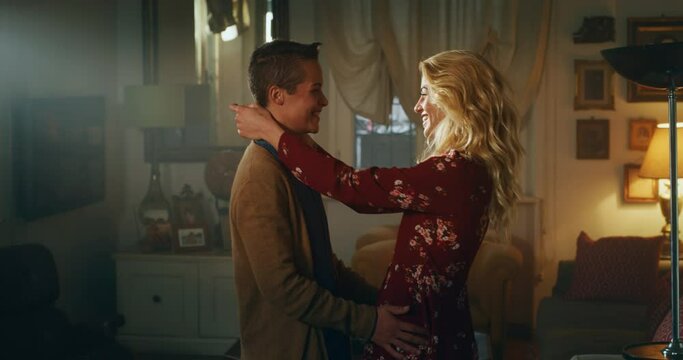 Cinematic shot of carefree happy homosexual female gay and transgender man couple in love is enjoying time together is hugging and kissing with affection as sign of timeless forever love at home.