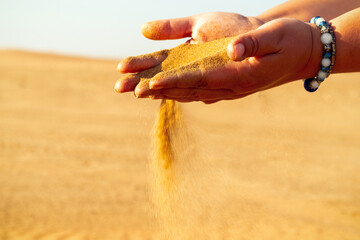 Close-up hand releasing dropping sand. Sand flowing through the hands against golden desert.