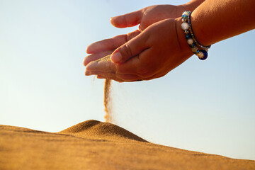 Close-up hand releasing dropping sand. Sand flowing through the hands against golden desert.