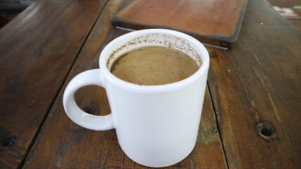 Hot coffee milk served on white mug and plastic glass on a wooden table.
