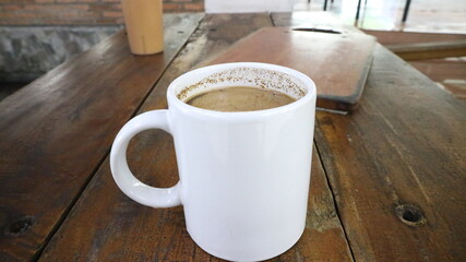 Hot coffee milk served on white mug and plastic glass on a wooden table.