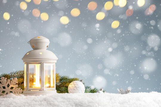 White lantern with christmas decorations in a snowdrift on blue background