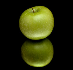 Green apple on reflective surface, isolated on black 

