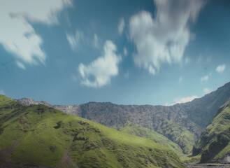 Fototapeta premium Nice hills covered by green grass above them clouds in blue sky. behind them rocks .