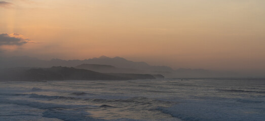 Naklejka na ściany i meble ocean coast at sunset with waves breaking and mountains in silhouette behind