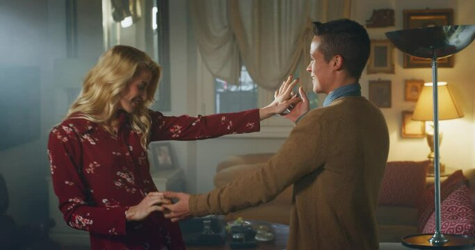 Cinematic shot of young carefree happy smiling homosexual female gay and transgender man couple in love is enjoying time together and having fun to dance together while listening to the music at home