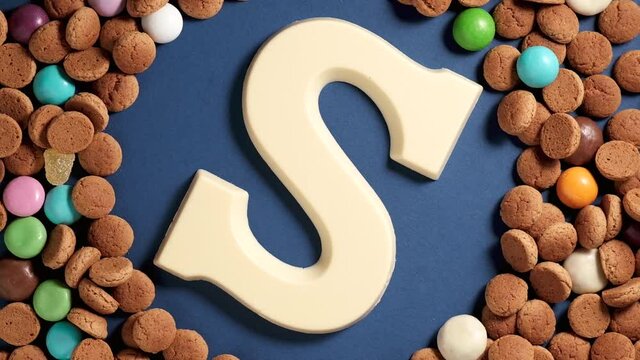 Rotation of kruidnoten, traditional sweets, strooigoed and white chocolate letter S. Background for Dutch holiday Sinterklaas. St. Nicholas day concept. FullHD video, top view