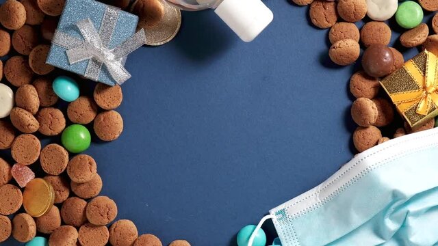 Overhead shot of Dutch holiday Sinterklaas Saint Nicholas day during covid-19 pandemic in Netherlands with kruidnoten cookies, traditional sweets, medical protective equipment. Rotating, copy space