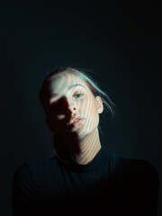 Fototapeta premium Portrait of beautiful young girl with a shadow pattern on her face in black dark studio
