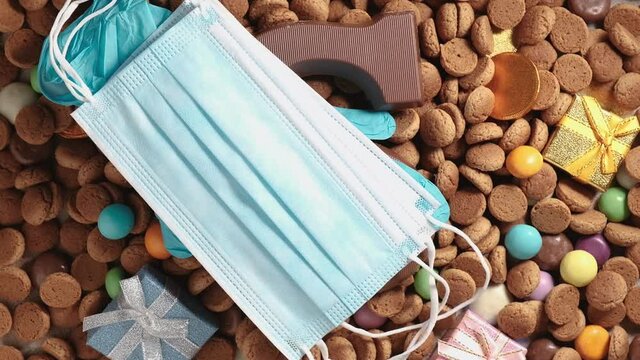 Women puts medical face mask and blue gloves on traditional dutch cookies kruidnoten. Overhead shot of Dutch holiday Sinterklaas Saint Nicholas day during covid-19 pandemic in Netherlands, rotating