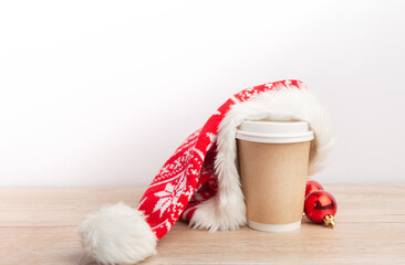 Obraz na płótnie Canvas paper cup of coffee wrapped in a santa hat on a white and wooden christmas background.
