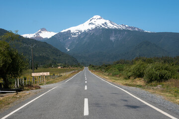 Fototapeta premium perspective sur route asphaltée en ligne droite avec une montagne enneigée surplombant la scène en arrière plan 