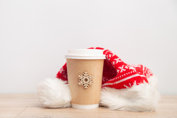 paper cup of coffee wrapped in a santa hat on a white and wooden christmas background.