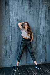 Fototapeta premium Caucasian girl in casual sportswear stands against the background of a gray wall in a loft studio. Sport and warm up