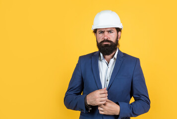 smart businessman in formal suit and safety helmet on yellow background with copy space, building