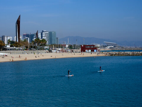 Vista panor&aacute;mica de una playa en Barcelona. Paddlers, edificios y espig&oacute;n.
