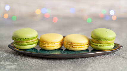 Green and yellow macaroons with pistachio and lime cream on brown wooden table and colored bokeh of Christmas garlands