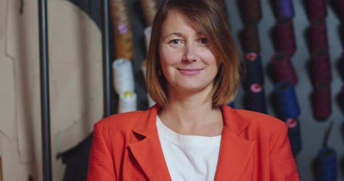 Close up portrait of beautiful young female entrepreneur standing in design studio in good mood. Cheerful Caucasian woman designer at office with smile on face in workshop with threads on background