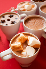 Close-up hot cocoa with marshmallows in white cups on red background, vertical