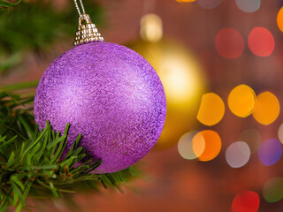 Purple christmas ball on christmas tree with garland blurred background