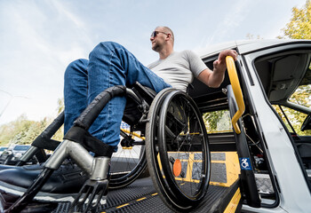 Fototapeta premium A man in a wheelchair on a lift of a vehicle for people with disabilities