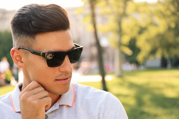 Handsome man wearing stylish sunglasses in park. Space for text