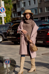 beautiful caucasian brunette woman in a stylish outfit walking down the street in the offseason in a coat and hat
